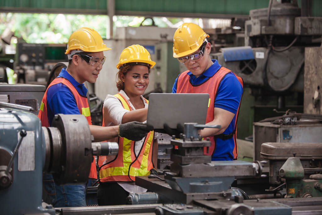 Equipe de profissionais analisando projeto em fábrica ao lado de torno horizontal